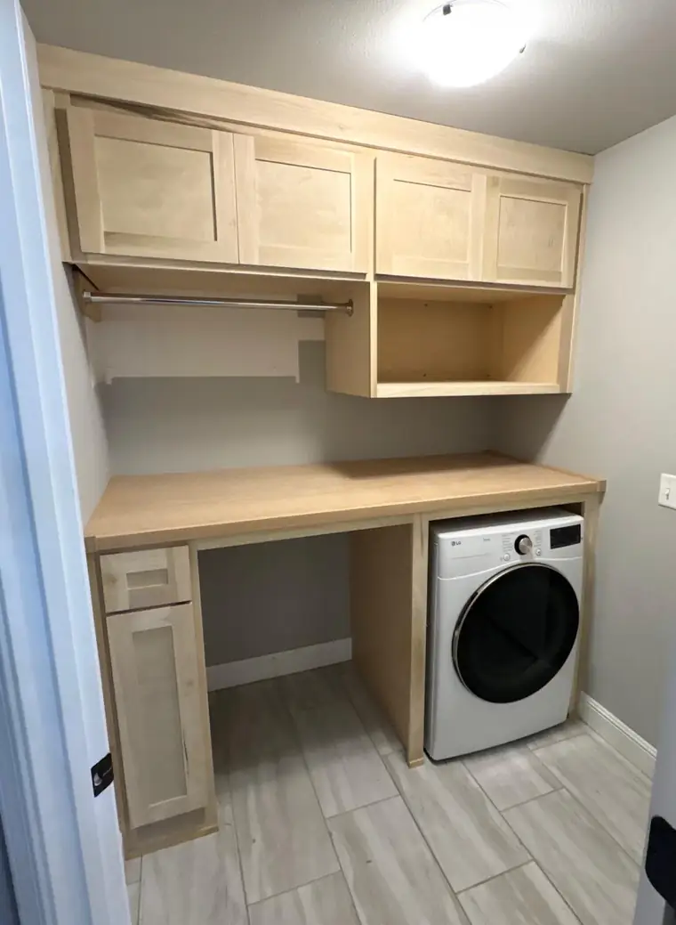 Light maple laundry room cabinets with a hanging rod and folding counter