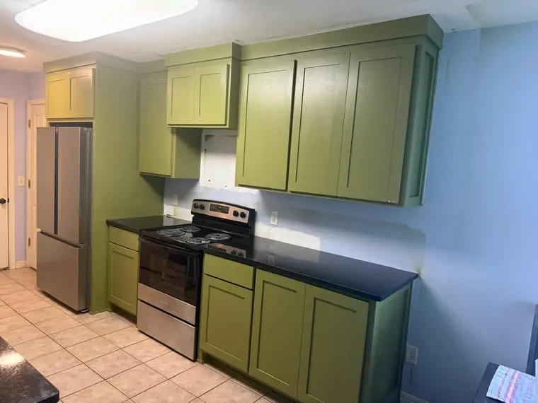 Olive green kitchen showing the full cabinet run and range wall