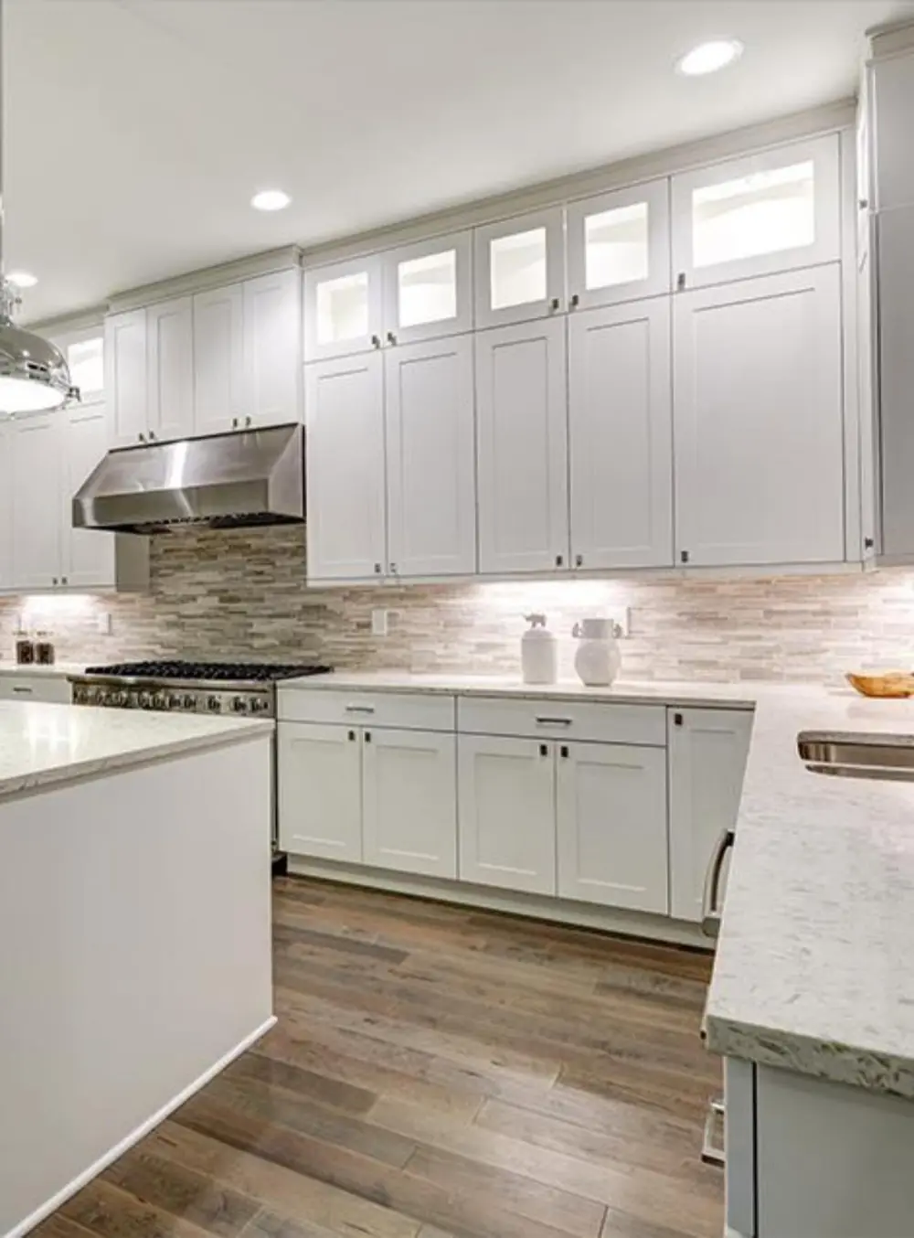 White painted cabinetry with glass transom uppers and stone backsplash
